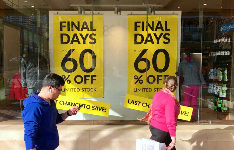 Shoppers walk past sales signs on display in the window
