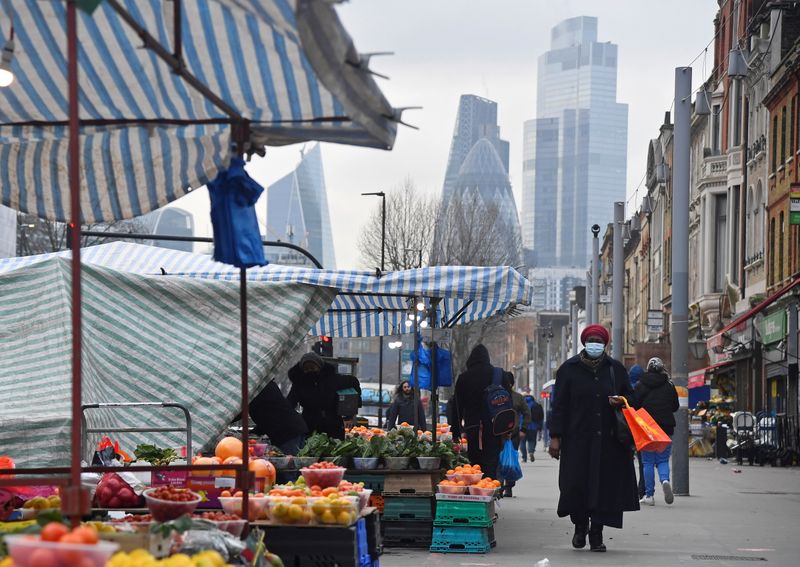 People shop at market stalls, with skyscrapers of the CIty