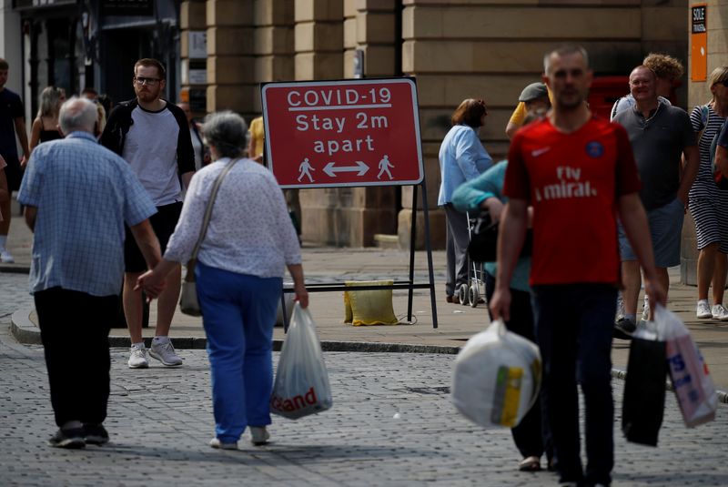 Shoppers walk past a social distancing sign following the outbreak