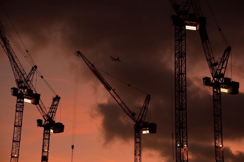 A plane flies behind cranes standing on construction sites at