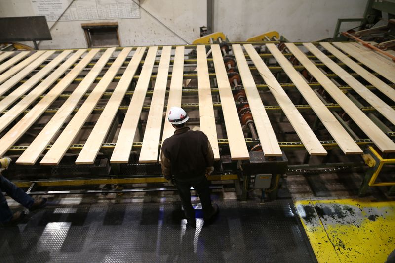 A worker inspects lumber on a conveyor belt at West