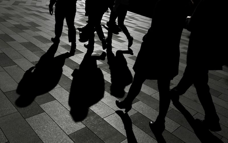 Workers cast shadows as they stroll among the office towers