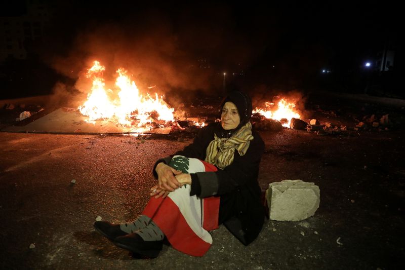 A demonstrator sits on the ground near burning fire during