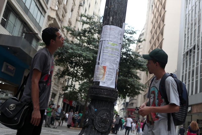 Young men look at job listings posted on a street