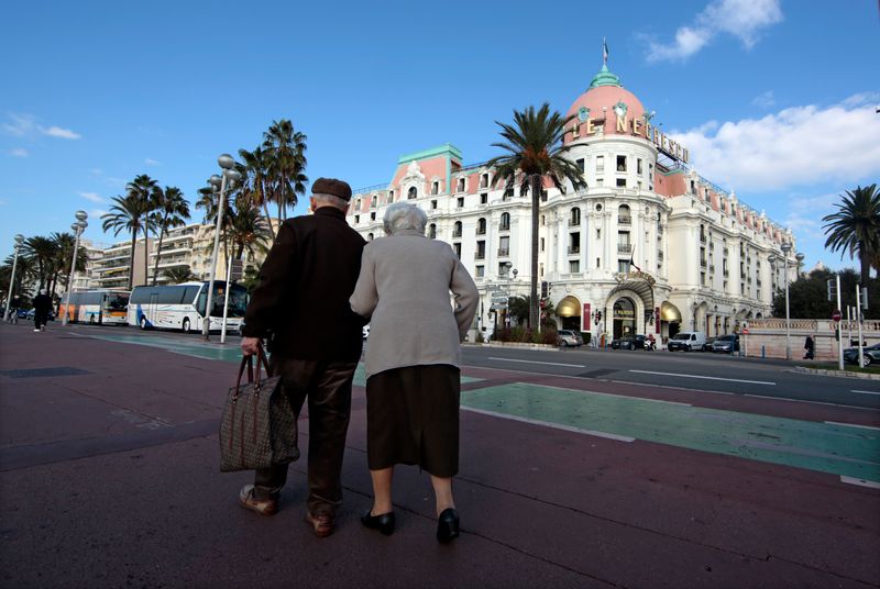 Two elderly people walk on the Promenade Des Anglais in