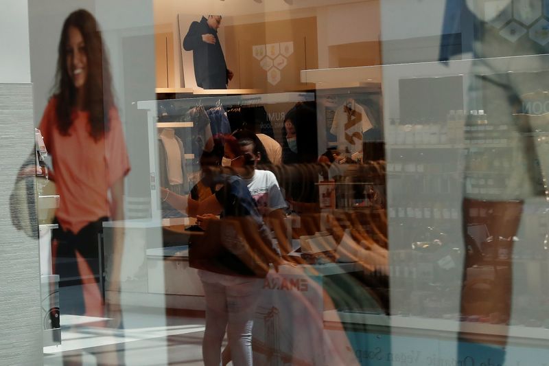 People are seen reflected in a storefront window shopping at