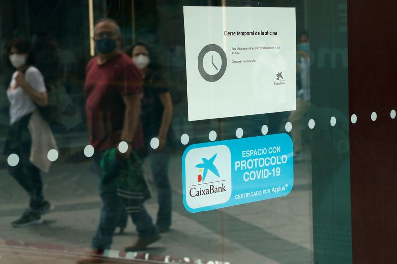 People walk past a closed Caixabank’s branch during a one-day