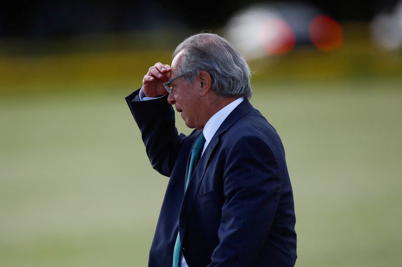 Brazil’s Economy Minister Paulo Guedes walks before a national flag