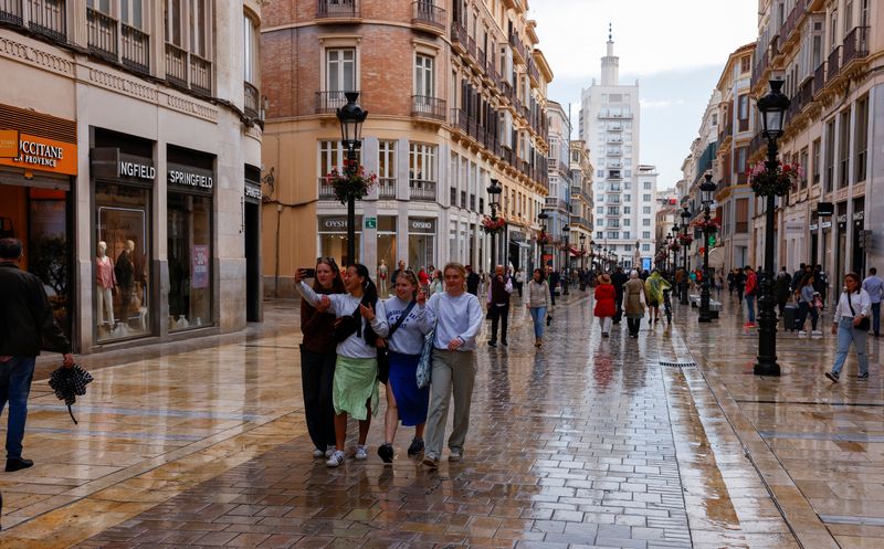 Tourists walk along a shopping street in central Malaga