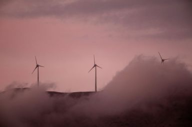Wind turbines operate atop a mountain during sunset near the