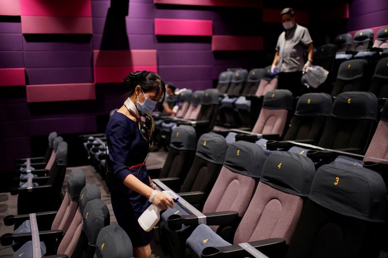 A staff member wearing a face mask disinfects seats in