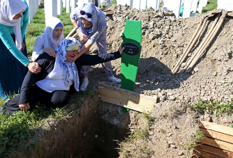 Women cry near the grave of their relative, who is