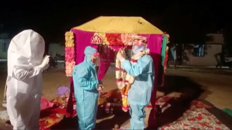 A bride and groom wearing PPE exchange flower garlands during
