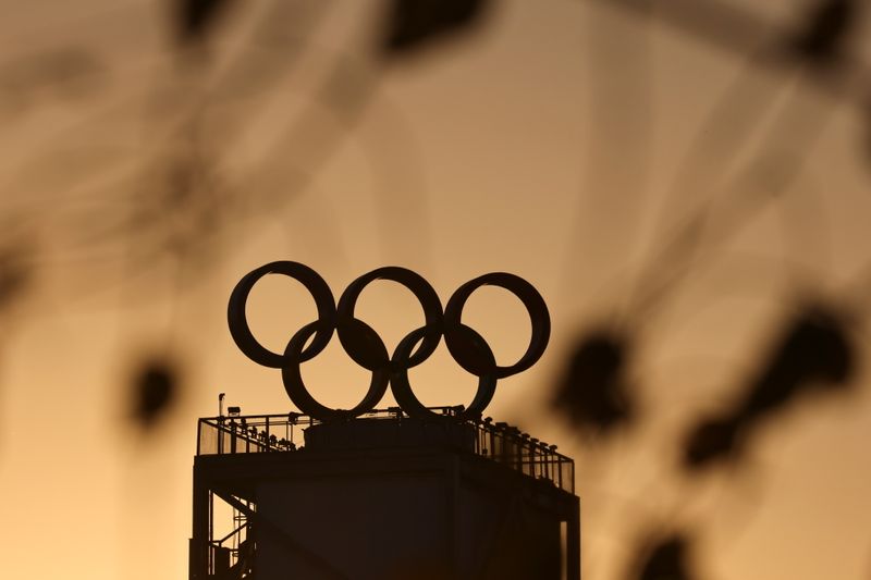 The sun sets behind a building topped with the Olympic