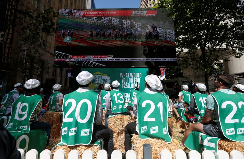 FILE PHOTO: Sports betters sit on ‘racehorses’ made from hay