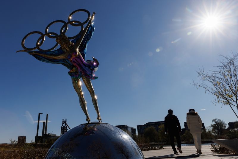 People walk past a sculpture featuring the Olympic rings outside