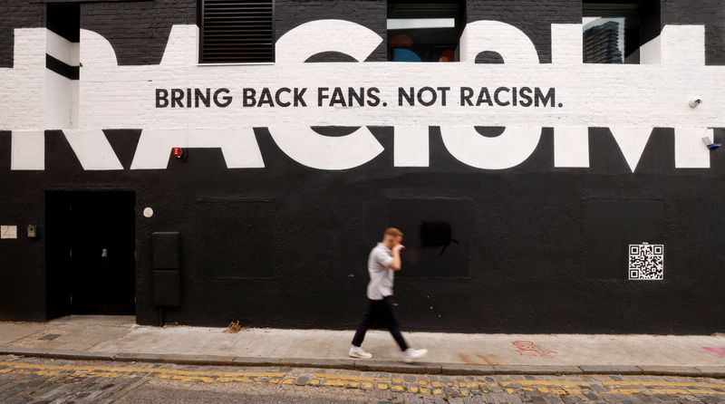 A man walks past sport-related anti-racism graffiti on the side