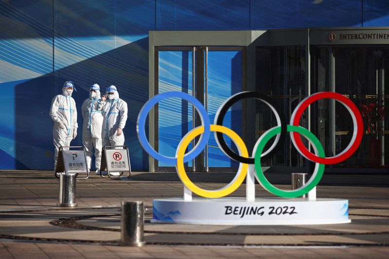 Workers in PPE stand next to the Olympic rings inside