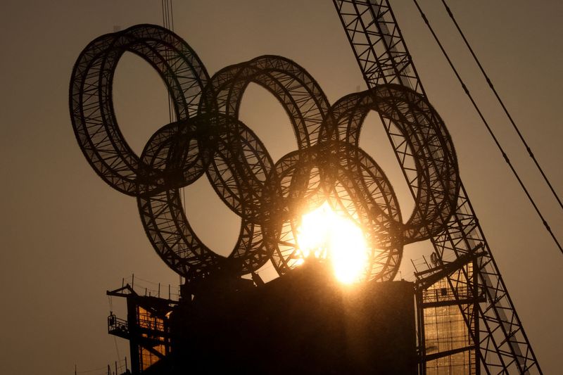 The sun sets behind the Olympic Rings atop a tower