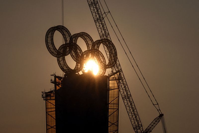 The sun sets behind the Olympic Rings atop a tower
