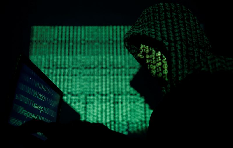 Hooded man holds a laptop computer as cyber code is