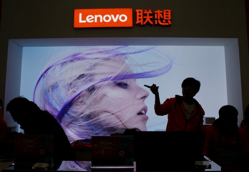 An employee gestures next to a Lenovo logo at Lenovo