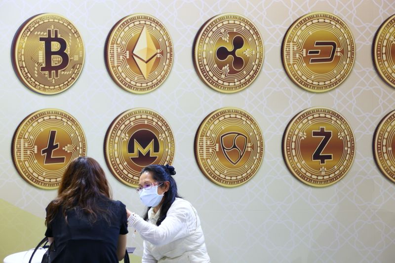 Customers talk against a backboard with signs of cryptocurrency during