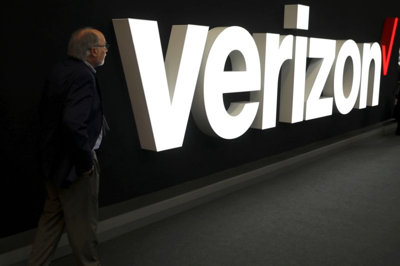 A man stands next to the logo of Verizon at