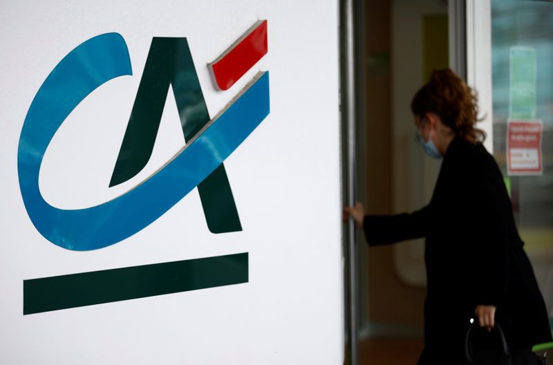 A woman walks past a Credit Agricole logo outside a