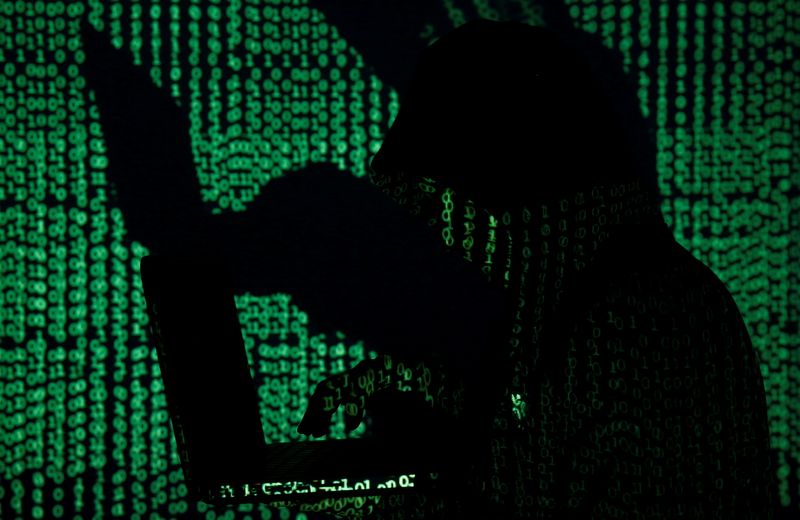 FILE PHOTO: Man holds laptop computer as cyber code is