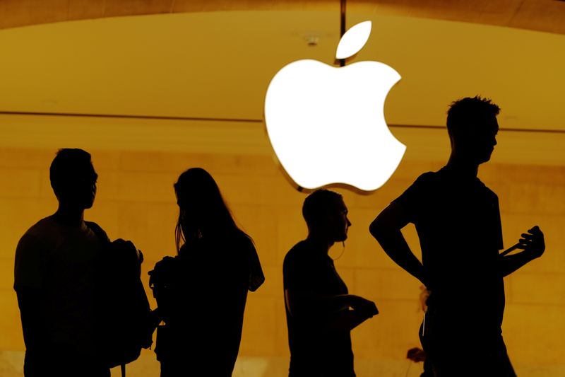 Customers walk past an Apple logo inside of an Apple