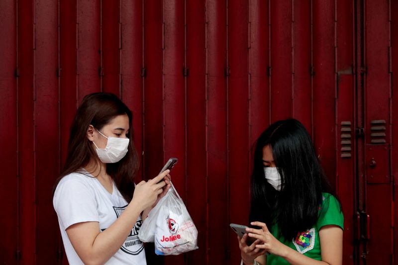 Women wearing face masks use their phones in Manila, Philippines