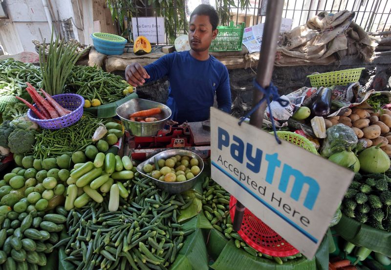 A vendor weighs vegetable next to an advertisement of Paytm,