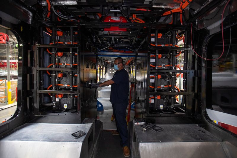 A worker installs electrical batteries in a bus at the