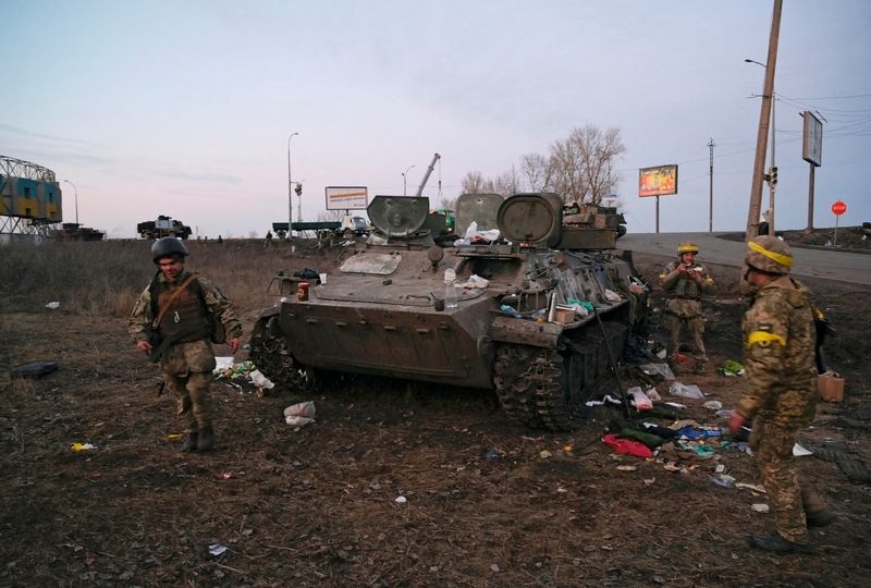 Ukrainian servicemen are seen next to a destroyed armoured vehicle,
