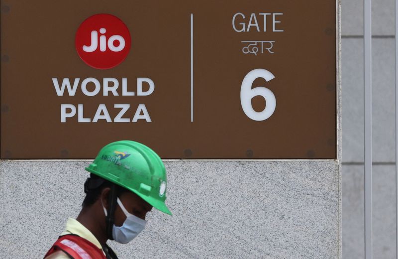 A construction worker walks past a gate of Reliance’s Jio