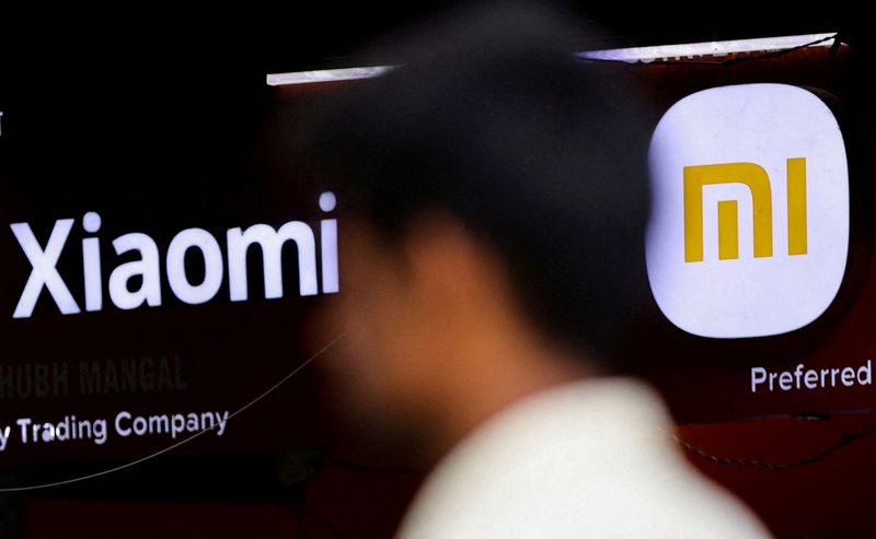 FILE PHOTO: A man walks past a logo of Xiaomi,