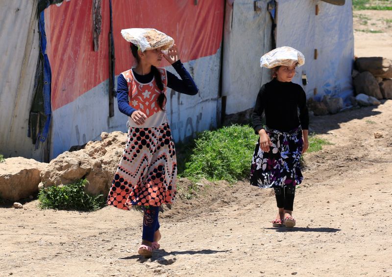 Syrian refugee girls carry stacks of bread on their heads,