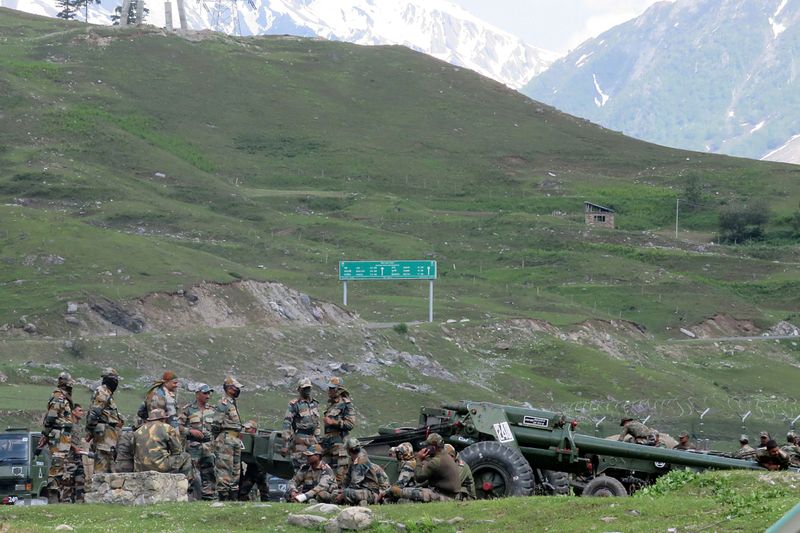 Indian army soldiers rest next to artillery guns at a