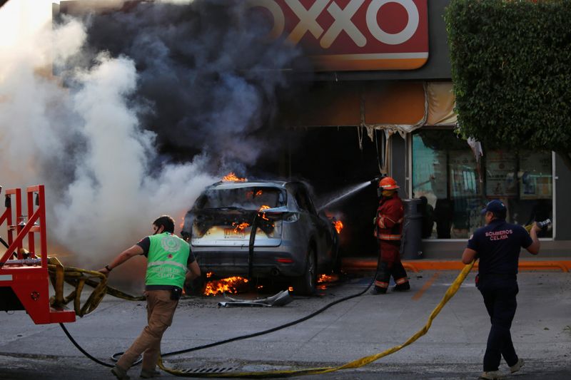 Firefighters work on a burning car outside a store after