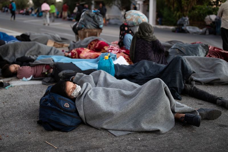 Refugees and migrants sleep on a road following a fire