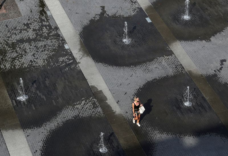 A woman walks among fountains on a square in central