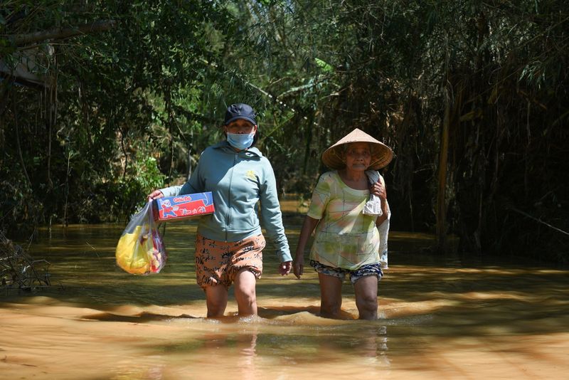 Women walk in a flooded road after their village was