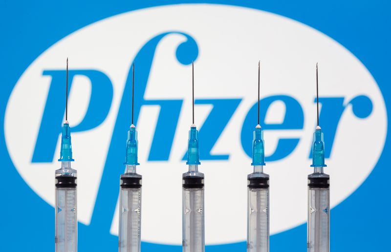 Syringes are seen in front of a displayed Pfizer logo
