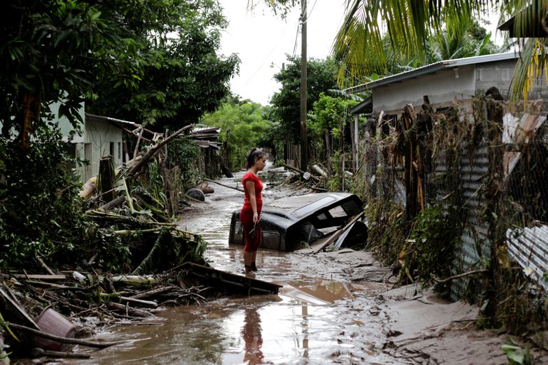 A woman stands outside her home damaged due to heavy