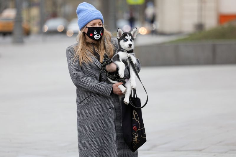 A woman wearing a protective face mask holds a dog