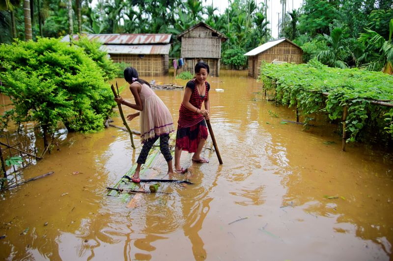 Girls row a makeshift raft past submerged houses at a