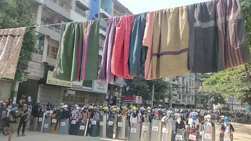 Traditional clothes hang on a rope as protesters holds shields