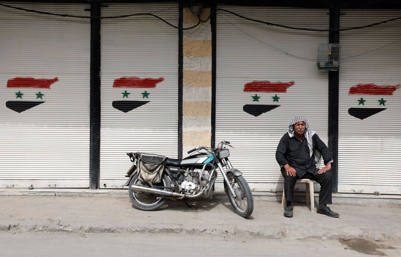 A man sits in front of closed shop with Syrian