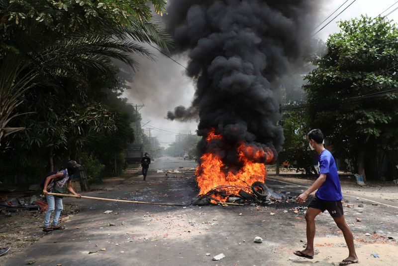 An anti-coup protester walks past burning tires, in Yangon